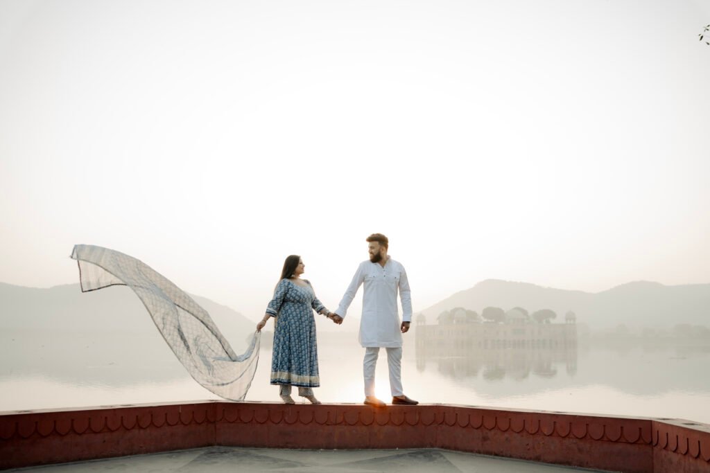 A romantic couple holding hands with a flowing dupatta during their Jal Mahal pre-wedding photoshoot at Man Sagar Lake in Jaipur.